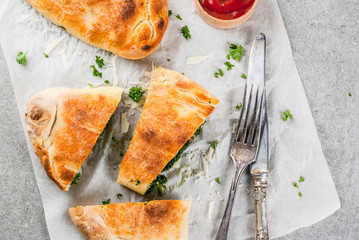 Italian food, closed pizza calzone with Spinach and Cheese, gray stone background, copy space top view