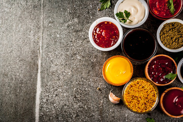 Set of different sauces - ketchup, mayonnaise, barbecue, soy, teriyaki, mustard, grain hills, pesto, adzhika, chutney, tkemali, pomegranate sauce on black stone background. Copy space top view