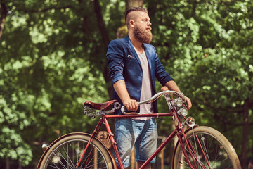 Male dressed in casual clothes, walking with a retro bicycle in a city park.
