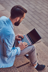A fashionable freelancer male with a full beard and haircut, wearing casual clothes, working on a...
