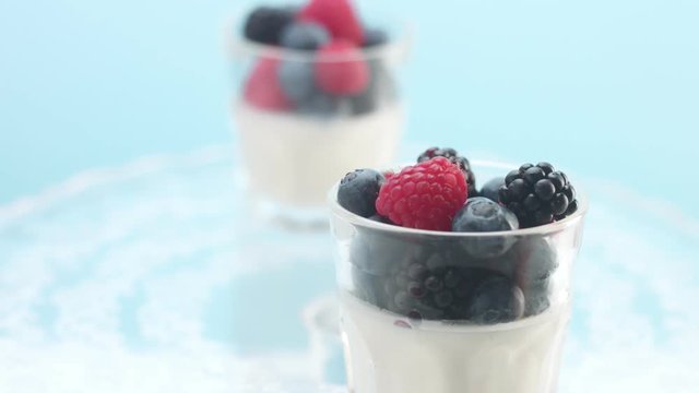 transparent glasses full of yogurt, panna cotta, white vanilla mousse decorated with berries on light blue. Brekfast with greek yogur and berries Minimalism food video