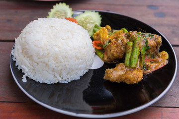 Stir fried red curry striped bass with rice in black dish on wooden table