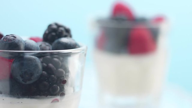 .changing focus to closest glass with panna cotta with berries and woman's hand picking up one raspberry Closeup minimalistic food lip