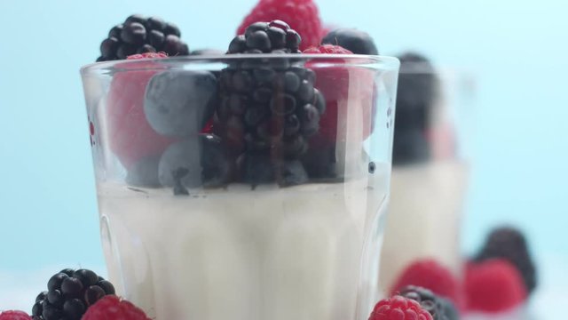 closeup of turning glasses with some white dessert mouse panna cotta yogurt decorated with berries on light blue background