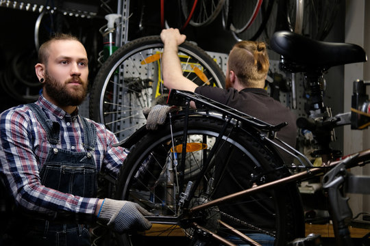 Two handsome stylish male working with a bicycle in a repair shop. Workers repair and mounts bike in a workshop