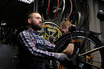 Fototapeta na wymiar Two handsome stylish male working with a bicycle in a repair shop. Workers repair and mounts bike in a workshop