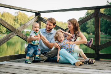 Fototapeta na wymiar Happy smiling Family Sitting On Wooden Jetty having fun and playing. Parents with cute kids outdoors