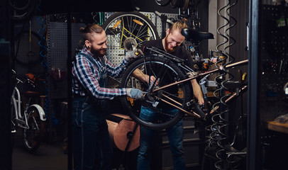 Two handsome stylish male working with a bicycle in a repair shop. Workers repair and mounts bike in a workshop