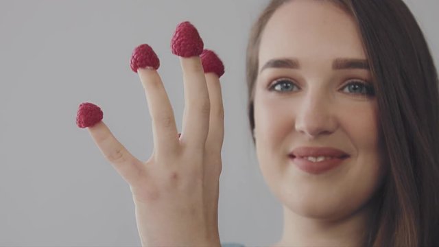 young caucasian woman with straight long hair eats raspberry from fingers. Hand with fingers with raspberry. Model have fun.