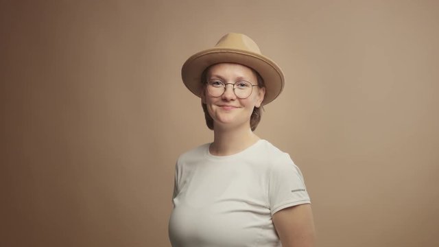 woman's portrait in studio wears a hat in beige background and looking at camera. Calm portrait lineal dolly zoom