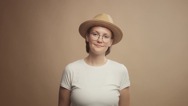 woman's portrait in studio wears a hat in beige background and looking at camera. Calm portrait lineal dolly zoom