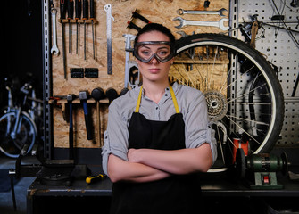 Portrait of a beautiful brunette female wearing working clothes, apron and goggles, standing in a workshop. 