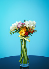 Glass vase with beautiful freesia on table against color background
