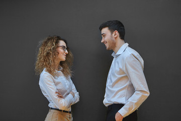 People, job, business and relations concept. Picture of two talented skillful young Caucasian creative people coworkers man and woman dressed in formal clothes having nice conversation at blank wall