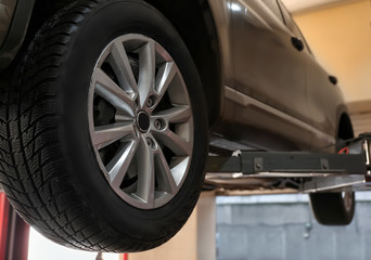 Car on hydraulic vehicle lift in garage, closeup. Tire service