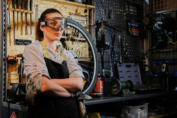 Fototapeta na wymiar Portrait of a beautiful brunette female wearing working clothes, apron and goggles, standing in a workshop. 