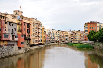 Naklejka na ściany i meble Colorful houses, reflected in the water of the river Onyar. View from the Red iron bridge or Girona Eiffel Bridge (Pont de les Peixateries velles). The historic Jewish quarter in Girona, Spain. 