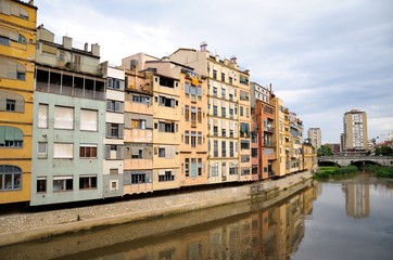 Fototapeta na wymiar Colorful houses, reflected in the water of the river Onyar. View from the Red iron bridge or Girona Eiffel Bridge (Pont de les Peixateries velles). The historic Jewish quarter in Girona, Spain. 