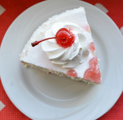  piece of a biscuit cake with white cream and a cherry berries on a plate isolated close-up, top view