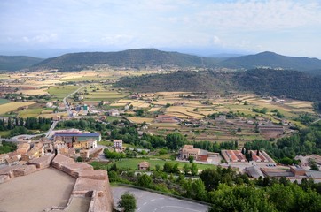View from Cardona Castle. Sunlit large valley with colorful fields and small houses. The valley is surrounded by green mountains. Blue sky and white clouds. Summer. Catalonia, Spain.