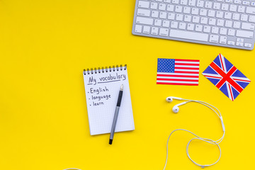 Learn english concept. British and american flags, computer keyboard, notebook for new vocabulary on yellow background top view copy space