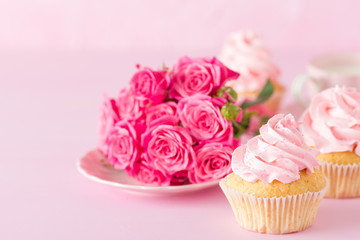 Cupcake with pink cream decoration and roses on pink pastel background.