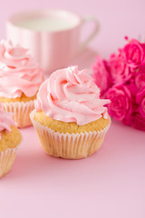 Cupcake with pink cream decoration and roses on pink pastel background.