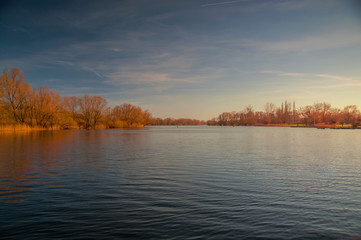 Fototapeta premium Panorama view of a lake with blue sky and golden sunset light. Südsee in Braunschweig, Germany