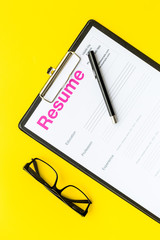 Looking for work concept. Resume on pad near pen and glasses on yellow background top view