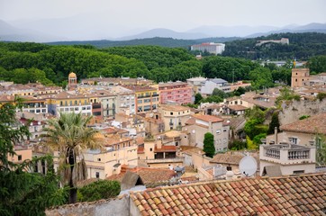 Fototapeta premium View of the city of Girona from the medieval pedestrian border wall. Roofs of houses, trees, mountains in a haze in the background. Cloudy sky. Girona, Spain