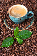 Cup of coffee with fresh coffee leaves on coffee beans background