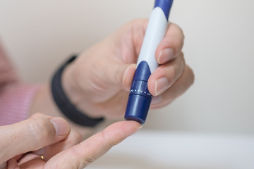 Close up of man hands using lancet on finger to check blood sugar level by Glucose meter using as Medicine, diabetes, glycemia, health care and people concept.