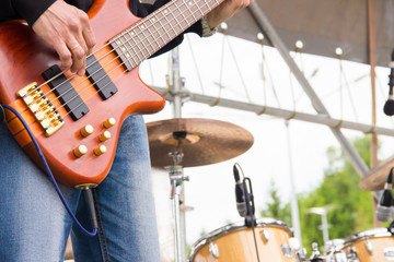 Musical band perfom on an open air festival. Bass guitarist man playing close, drums blurred