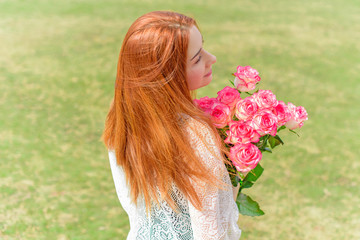 Pretty girl in a tender knitted dress, holding her hands on her shoulder a bouquet with pink roses on the background of garden 