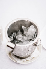 A bucket of ice cubes stands on a white background of the table. Close up.