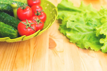 Fresh vegetables cucumbers and tomatoes in a green bowl on a wooden table next to green lettuce leaves. Vegetarian diet. Healthy diet and lifestyle