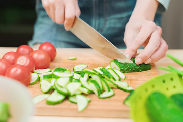 close-up of female hands cut into fresh cut cucumbers on a wooden cutting board next to pink tomatoes. The concept of homemade vegetarian cuisine and healthy eating and lifestyle
