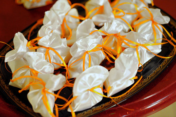 Small white pouches with orange ribbon on a tray. Pouches with gifts for guests at the wedding.