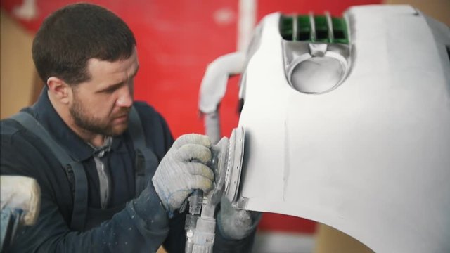 Man worker in uniform polishing car in a car-washing facility