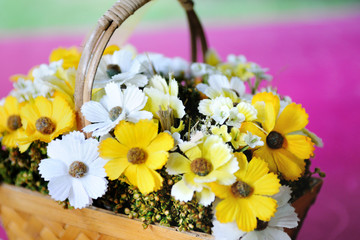 White and orange artificial flowers in a wicker basket.