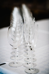 Empty glass for wine and champagne stand on white table. Close up. Empty glasses for elite drinks stand in two rows.