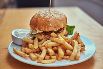 Close-up image of a hamburger with French fries and spicy sauce on a white plate. Unhealthy food concept
