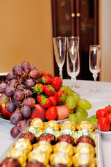 Fruits and berries on a platter, candy and glasses on a white table. Snacks on a buffet table.