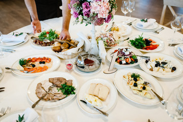 The waiter serves a dinner on a festive table. Food, Salads, Meat, Fish Meals. Festive table at wedding banquet. Artwork. Decor. Details.
