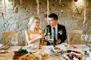 Newlyweds holding glasses of champagne to toast on hands of the indoors. Wedding ceremony decorated...