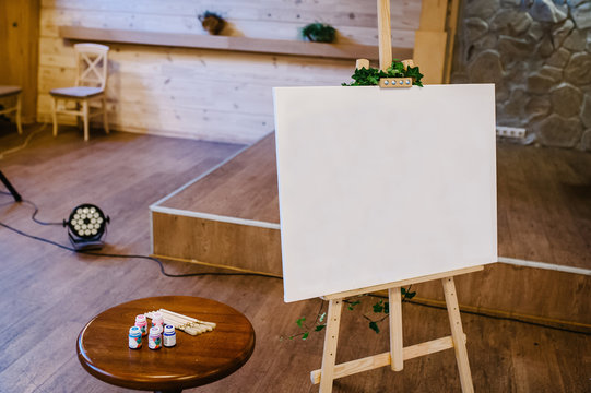 Clean easel with paint brush. White Easel with the image of human faces indoor. art, creativity.
