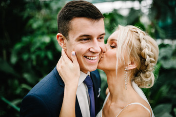 Newlyweds are standing and kissing in the Botanical green garden full of greenery. Wedding ceremony.