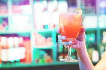 selective soft focus with dramatic lighting of A woman hand holding glass beverage alcohol drinking cocktail fruit juice mix. background bar colorful light