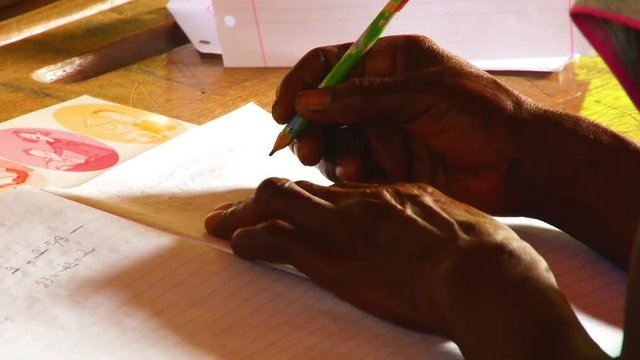 Close up of an older African woman attempting to write in a notebook in a classroom in Africa