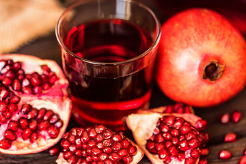 Ripe pomegranates with glass of juice on table